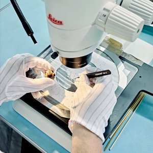 Person prüft ein Bauteil unter einem Mikroskop